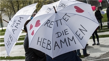 Zwei Frauen tragen am 12.04.2014 in Berlin bei einem Protestumzug für den Erhalt der freien Geburtenhilfe Regenschirme mit der Aufschrift "Rettet die Hebammen".