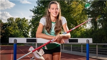 Leichtathletin Tamina Heller stützt sich an einer Hürde ab und hält einen Speer in der Hand. 