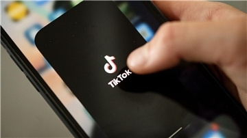 Ein Teenager tippt auf das TikTok-Logo auf einem Smartphone. 