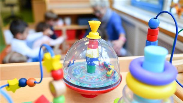 Kindergartenspielzeug in Nahaufnahme. Dahinter sieht man Kinder mit einer Erzieherin.
