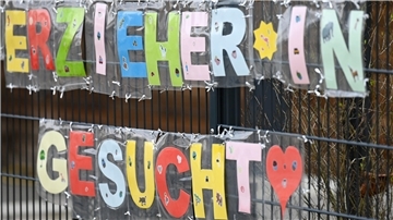 Mit bunten Buchstaben sind die Worte "Erzieher*in gesucht" an einem Zaun einer Kindertagesstätte befestigt.