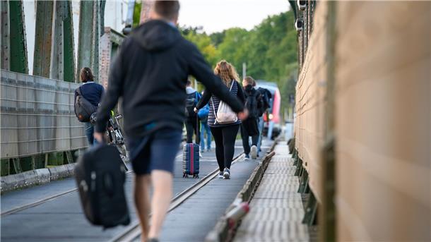 Fahrgäste laufen mit Koffern und anderem Gepäck über die Schleibrücke bei Lindaunis.