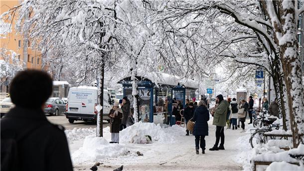 Fahrgäste warten an einer verschneiten Haltestelle auf einen Bus.