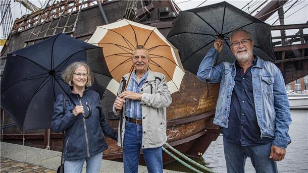 Drei Menschen im Regen mit Regenschirmen. 