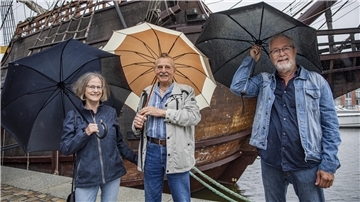 Drei Menschen im Regen mit Regenschirmen. 