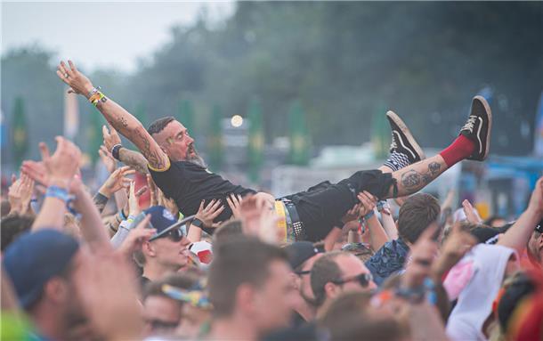 Deichbrand 2023: Magische Momente auf und vor den BÜHNEN (Fotos) Festivalbesucher stimmen in den Punkrock der Band Rogers vor der Firestage ein. Und ein Festivalbesucher schwebt über der Menschenmenge.