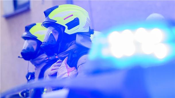 Hohe Rauchsäule bei Brand auf Recyclingbetrieb Feuerwehrleute stehen an einem Einsatzort.