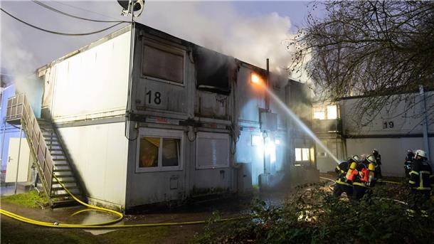 Feuerwehrleute stehen bei Löscharbeiten vor den verqualmten und teils brennenden Container-Einheiten einer Flüchtlingsunterkunft in Hamburg-Winterhude.