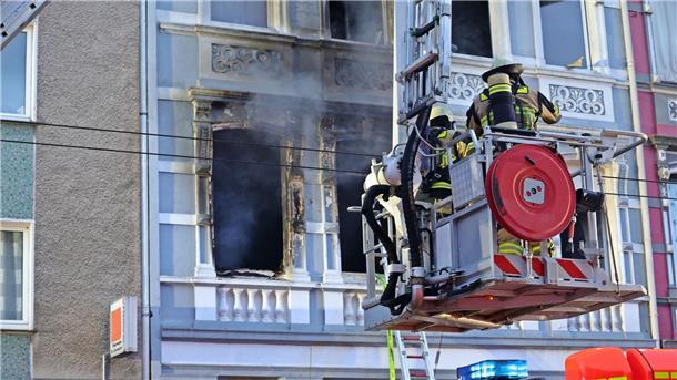 Solingen: Familie mit zwei Kindern stirbt bei Brand Feuerwehrmänner stehen vor dem Mehrfamilienhaus in Solingen; Rauch dringt aus einem der Fenster.