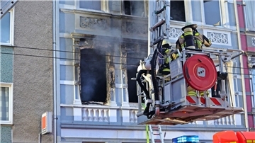 Feuerwehrmänner stehen vor dem Mehrfamilienhaus in Solingen; Rauch dringt aus einem der Fenster.