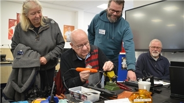 Filigranes Handwerk: Werner Abed (sitzend) schwingt Lötkolben und Schraubenzieher, Gaby Momberg-Greschke (von links), Philipp Tenhaef und Werner Brunkhorst beobachten interessiert die Reparatur.