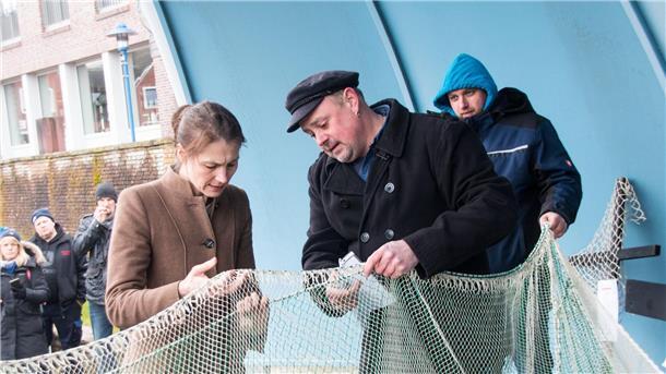 Fischer Nils Sander (M) zeigt Miriam Staudte (Bündnis 90/Die Grünen, l), Landwirtschaftsministerin von Niedersachsen, nach einem Treffen im Hafen Maschengrößen eines Netzes.