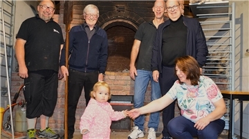 Vier Männer, eine Frau und ein Kind stehen vor einem Steinbackofen.