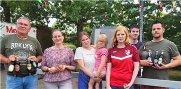 Sieben Menschen stehen lächelnd nebeneinander auf dem Parkplatz einer Turnhalle. 