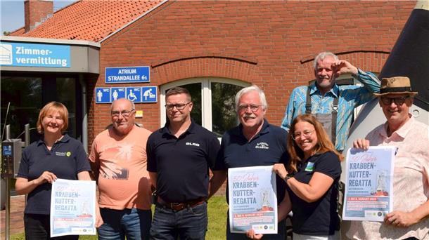 Mehrere Menschen stehen in einer Reihe. Einige von ihnen halten das Poster für die kommende Kutterregatta 2024 in der Hand. 