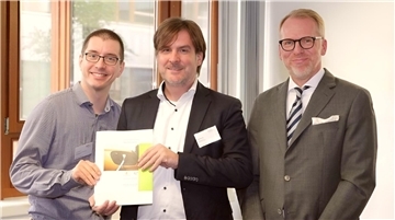 Drei Männer, davon halten zwei ein Konzept in der Hand