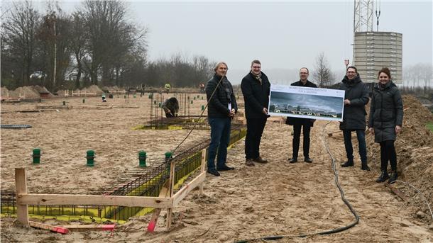 Eine Menschengruppe hält ein Plakat auf einer Baustelle hoch.
