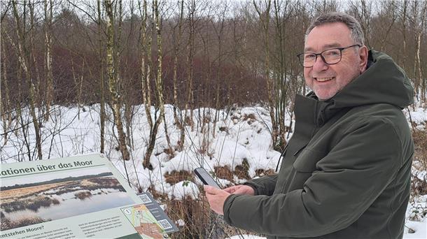 Friedrich Zittlosen ist beim Kultur- und Heimatverein Burg zu Hagen für das Königsmoor verantwortlich. Mit seinem Smartphone ruft er einen QR-Code am Rundweg die Geschichte von Piepenbrinks Hochszeit auf.