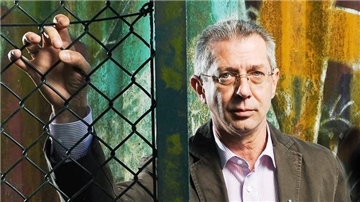 Ein Mann mit grauen Haaren steht vor einer bunten Wand.