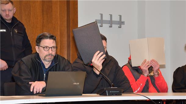 Zwei Männer verdecken mit Mappen ihr Gesicht.