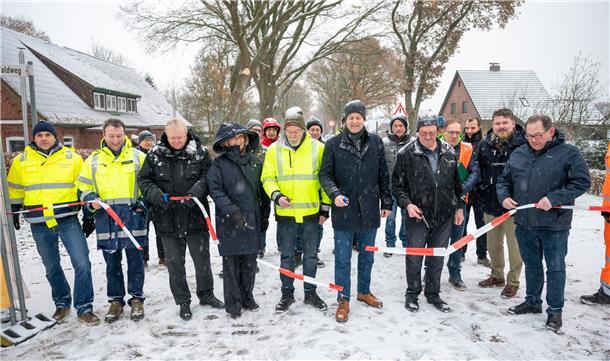 Eine Gruppe von Männern und eine Frau stehen im Schnee auf der Straße und durchschneiden ein Band.
