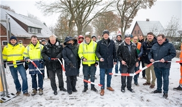 Eine Gruppe von Männern und eine Frau stehen im Schnee auf der Straße und durchschneiden ein Band.