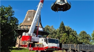 Ein Autokran hebt die Haube einer Galerieholländer-Windmühle ab