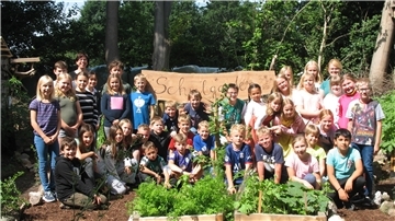 Die Schüler der Grundschule Elsdorf stehen vor dem Schild zum Eingang des Schulgartens.