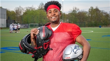 Ein Footballspieler steht auf dem Feld und hält seine Ausrüstung in der Hand.