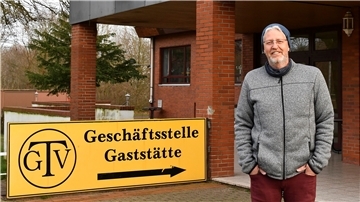 Ein Mann steht vor einem Haus und einem Schild. 