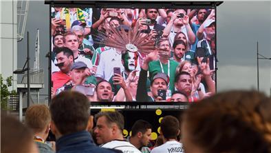 Menschen schauen gemeinsam auf einer großen Leinwand Fußball. 