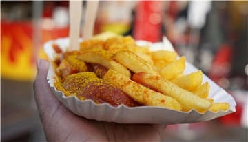 Eine Hand hält eine Papp-Schale mit Pommes und Currywurst.