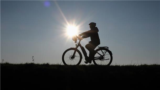 Gegen die Sonne fotografiert sieht man die Silhouette eines Fahrradfahrers.