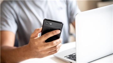 Ein Mann mit einem Handy und Laptop. 