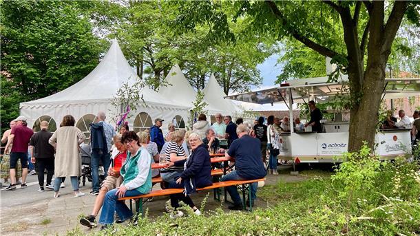 Menschen sitzen und stehen vor einem Festzelt. 