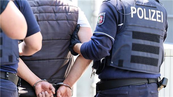 Polizisten führen einen Mann in Handschellen ab.