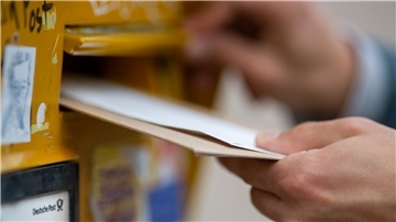 Ein Mann wirft Briefe in einen Briefkasten.