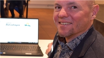 Ein Mann schaut in die Kamera, neben ihm ist ein aufgeklappter Laptop zu sehen.