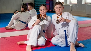 Die Karate-Geschwister Dana und Maxim Haak sitzen auf der Tatami und halten ihre Medaillen in die Höhe. 