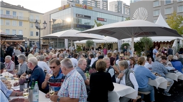 Viele Leute essen und trinken draußen an langen Tischen. 