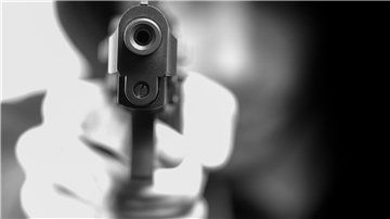 Ein Mann (unscharf im Hintergrund) hält eine Waffe in der Hand.