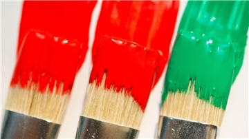 Pinsel mit roter, roter und grüner Farbe liegen auf einem weißen Blatt Papier. 
