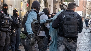 Polzisten führen einen mit einer Decke umhüllten Mann ab. 