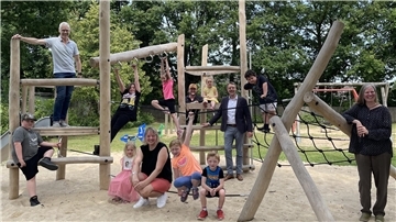 Kinder und Erwachsene auf einem Spielplatz mit neuen Geräten.
