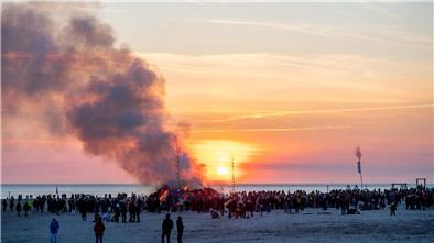 Rauch steigt auf über einem Osterfeuer am Meer.