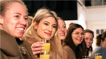 Mehrere Personen prosten sich mit einem Glas Organgensaft zu.