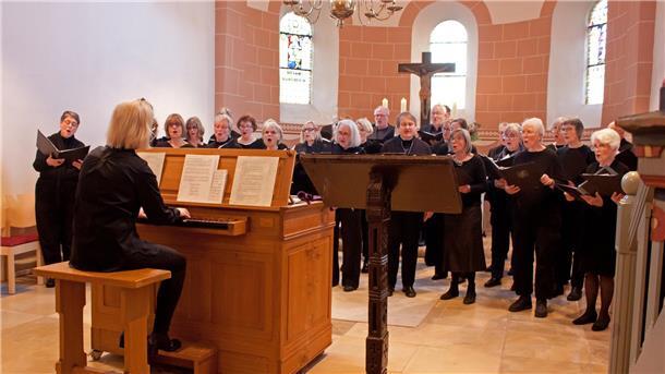 Eine Frau sitzt in einer Kirche an einer Orgel. Ihr steht ein Chor gegenüber und singt. 