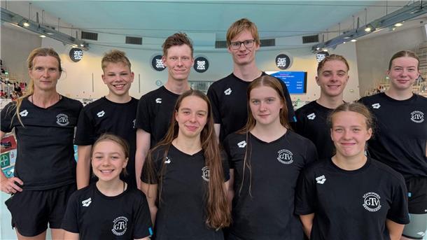 Ein Schwimmteam in schwarzen T-Shirts posiert für die Kamera.
