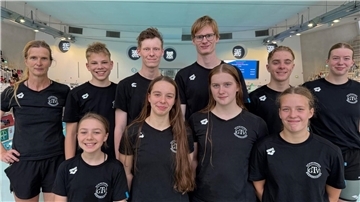 Ein Schwimmteam in schwarzen T-Shirts posiert für die Kamera.