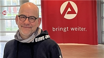 Mann lächelt im Hintergrund ist ein rotes Arbeitsagenturschild und die Worte" bringt weiter" zu lesen
